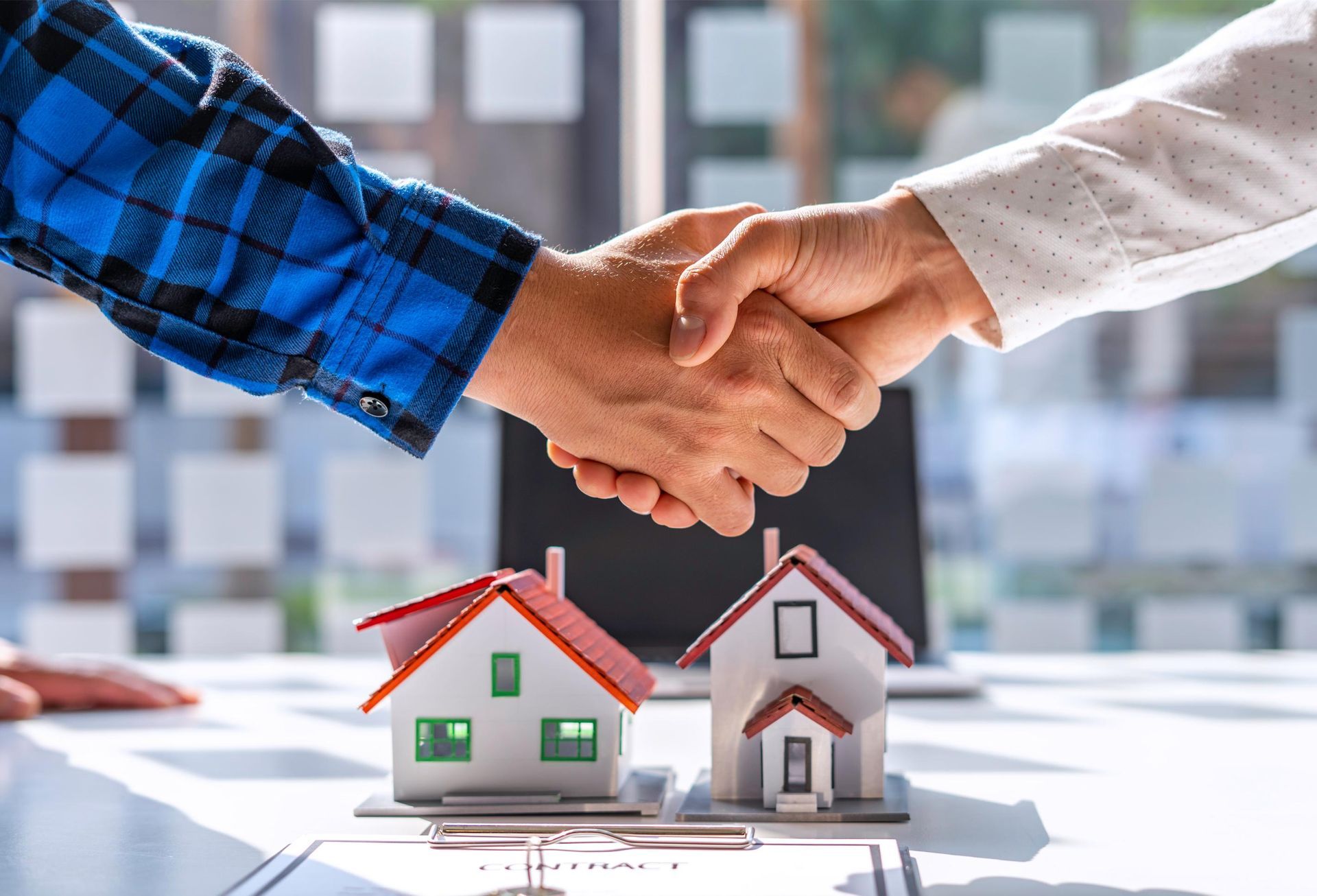 Two people shaking hands over miniature houses and contract.