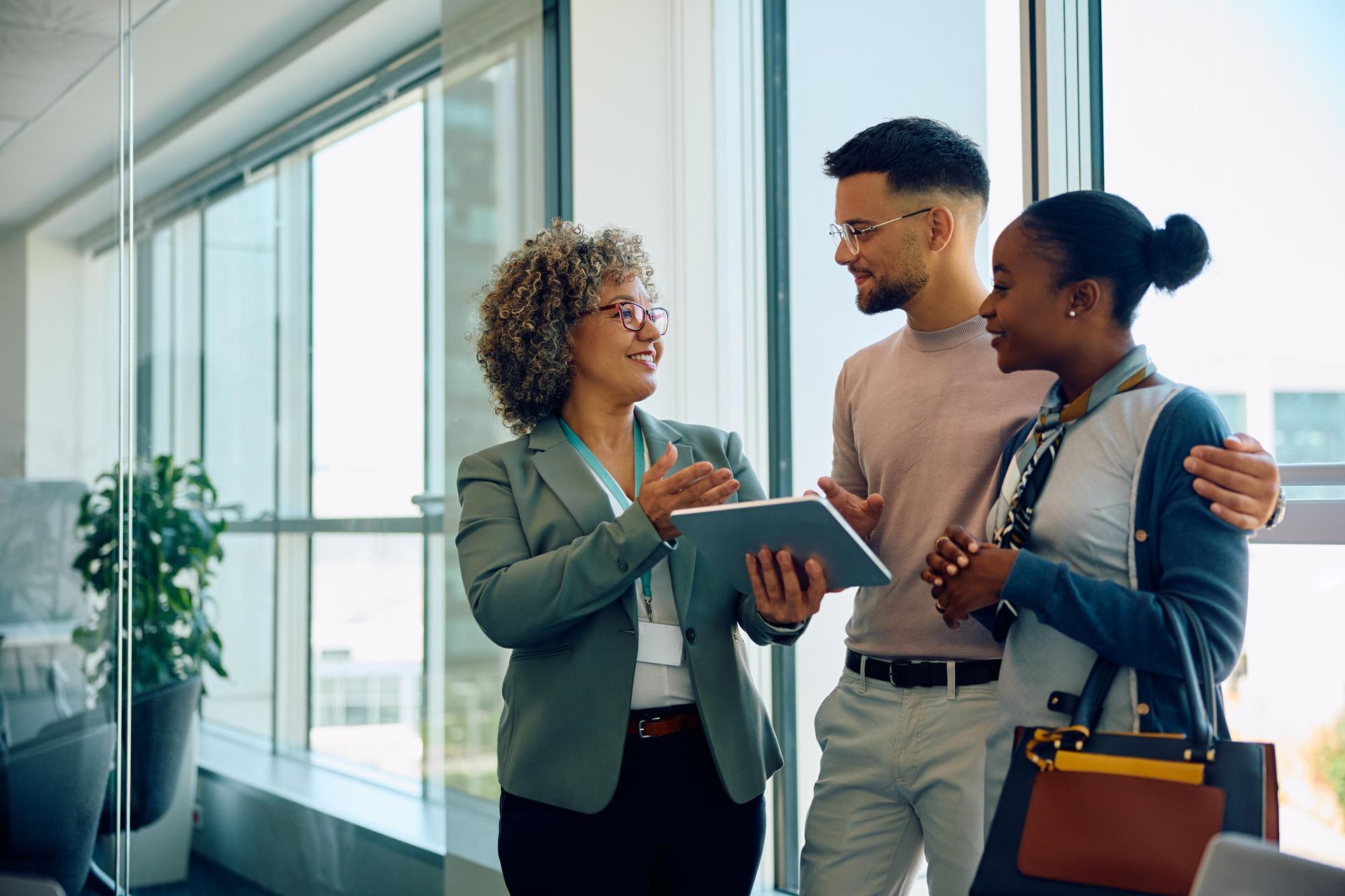 Real estate agent showing tablet to a couple in a bright office.