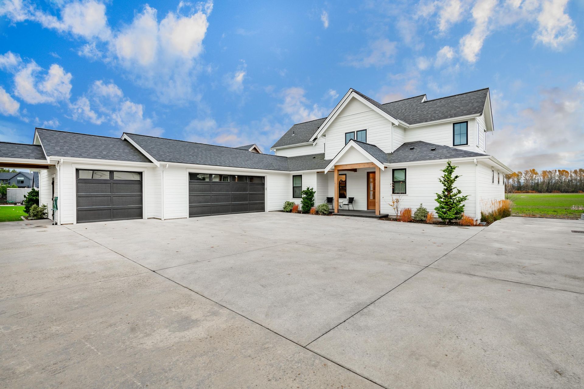 White farmhouse with black garage doors, concrete driveway, and blue sky.