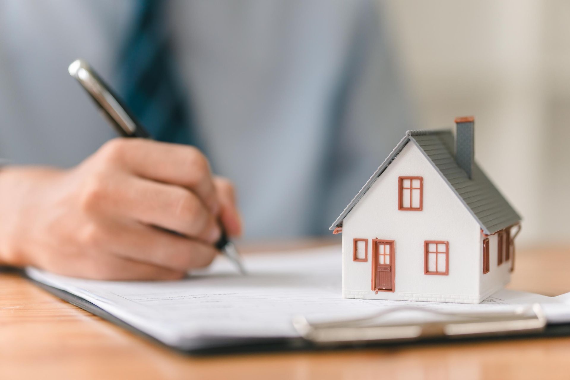 Person signing document with pen next to a miniature house on a desk.