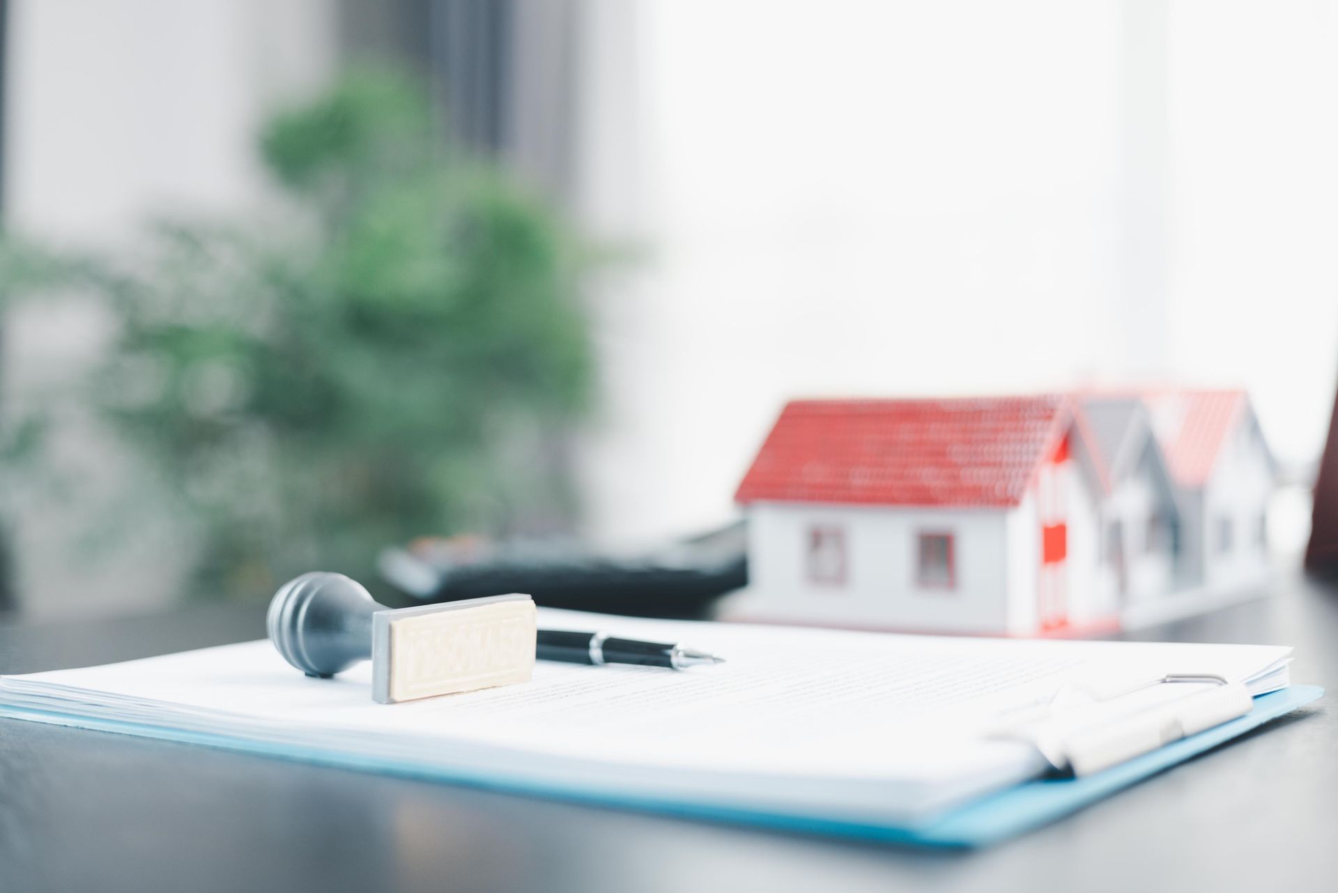 Real estate paperwork with a stamp, pen, and house model on a desk.