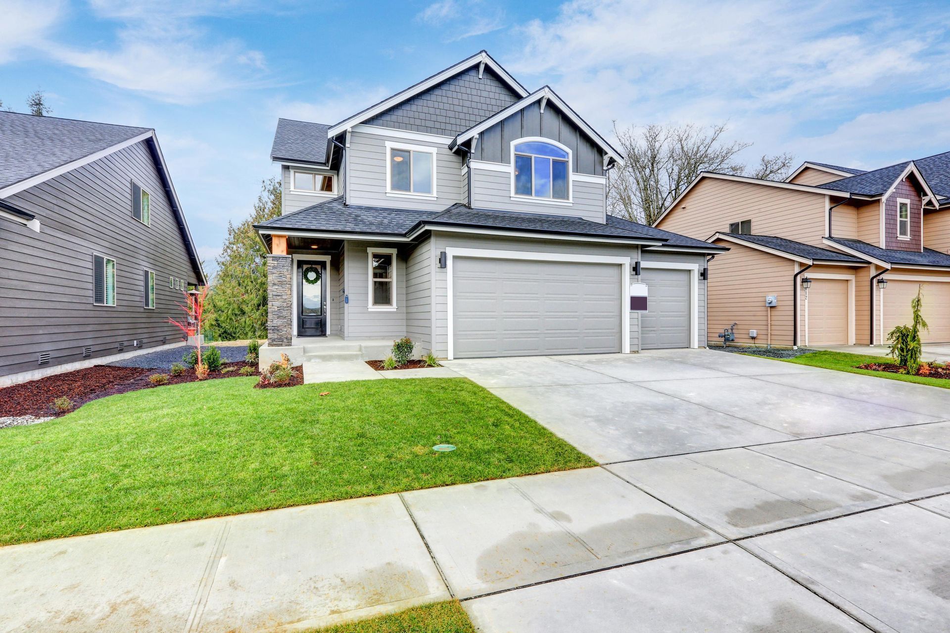 Two-story gray house with garage, green lawn, and concrete driveway on a sunny day.