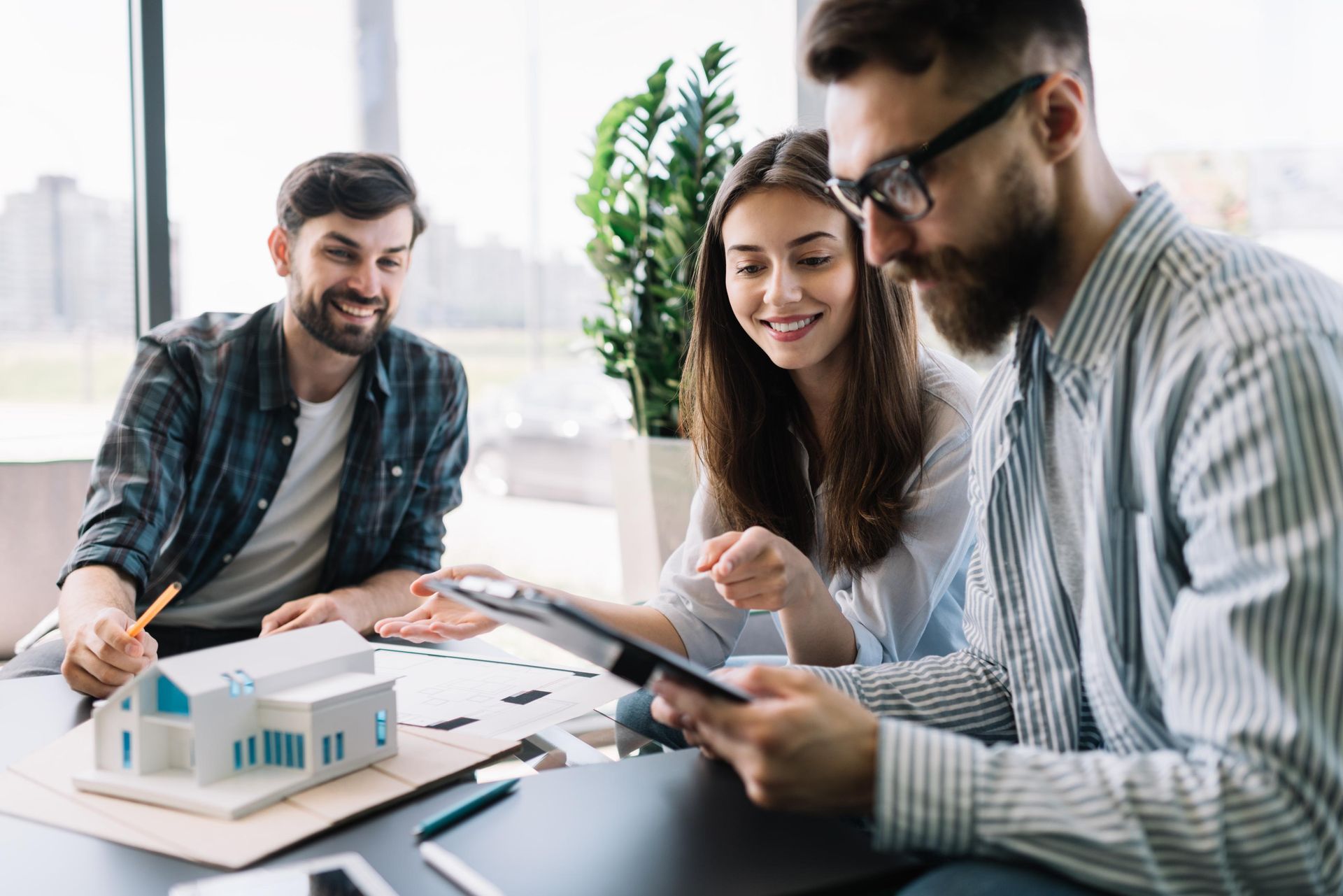 Three people review documents at a desk with a house model.