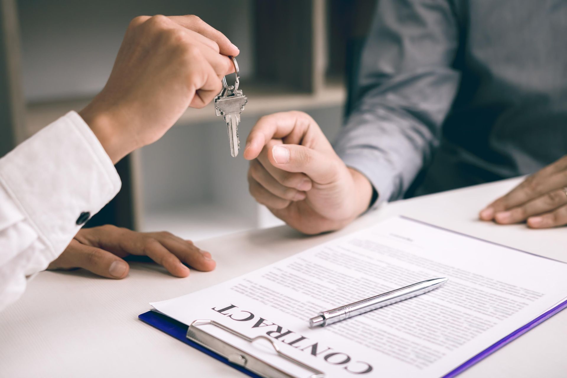 Person handing keys to another person over a contract document.
