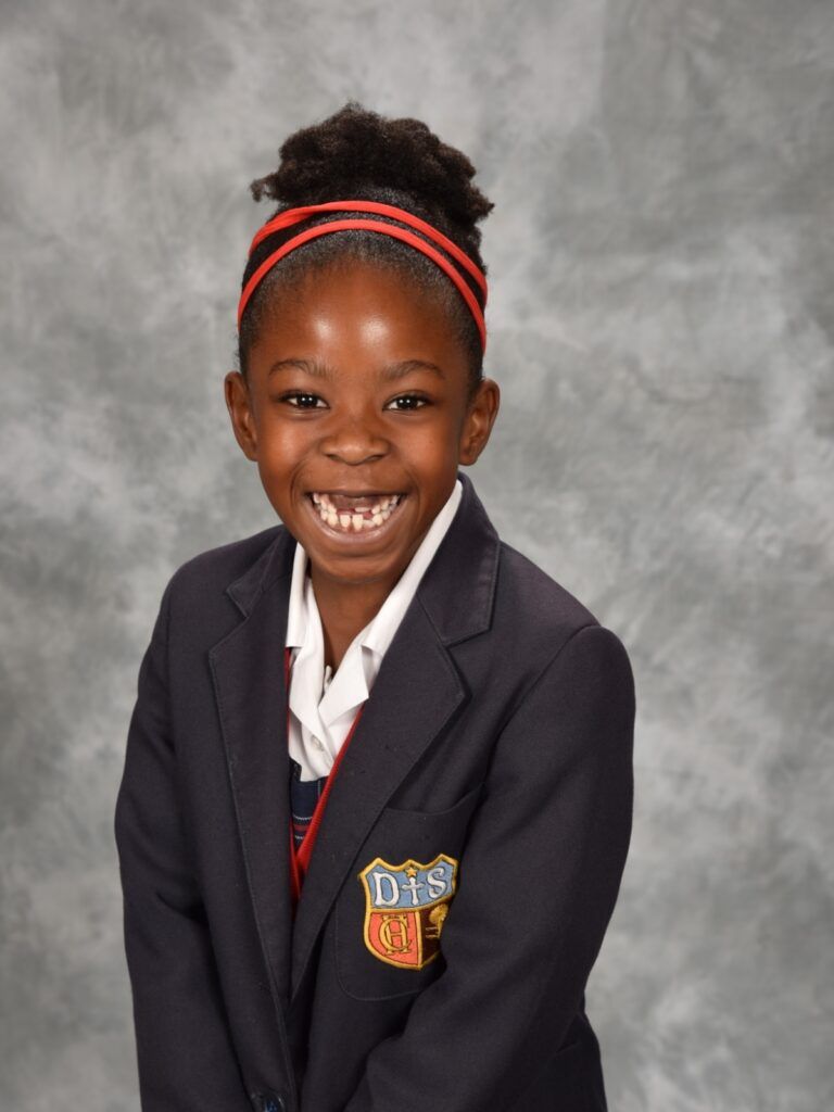 A young girl in a school uniform is smiling for the camera