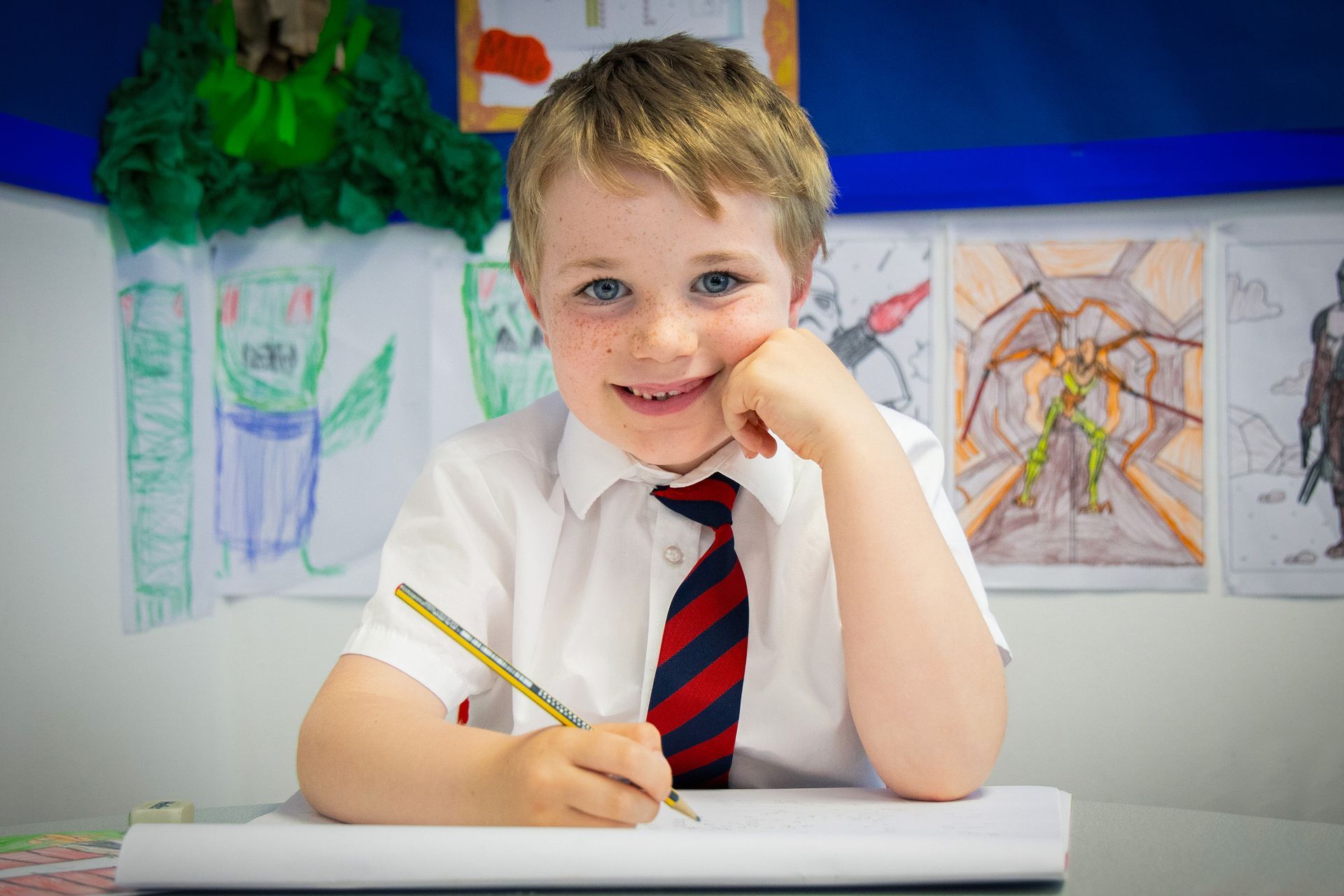A young boy is sitting at a desk in a classroom with a pencil in his hand.