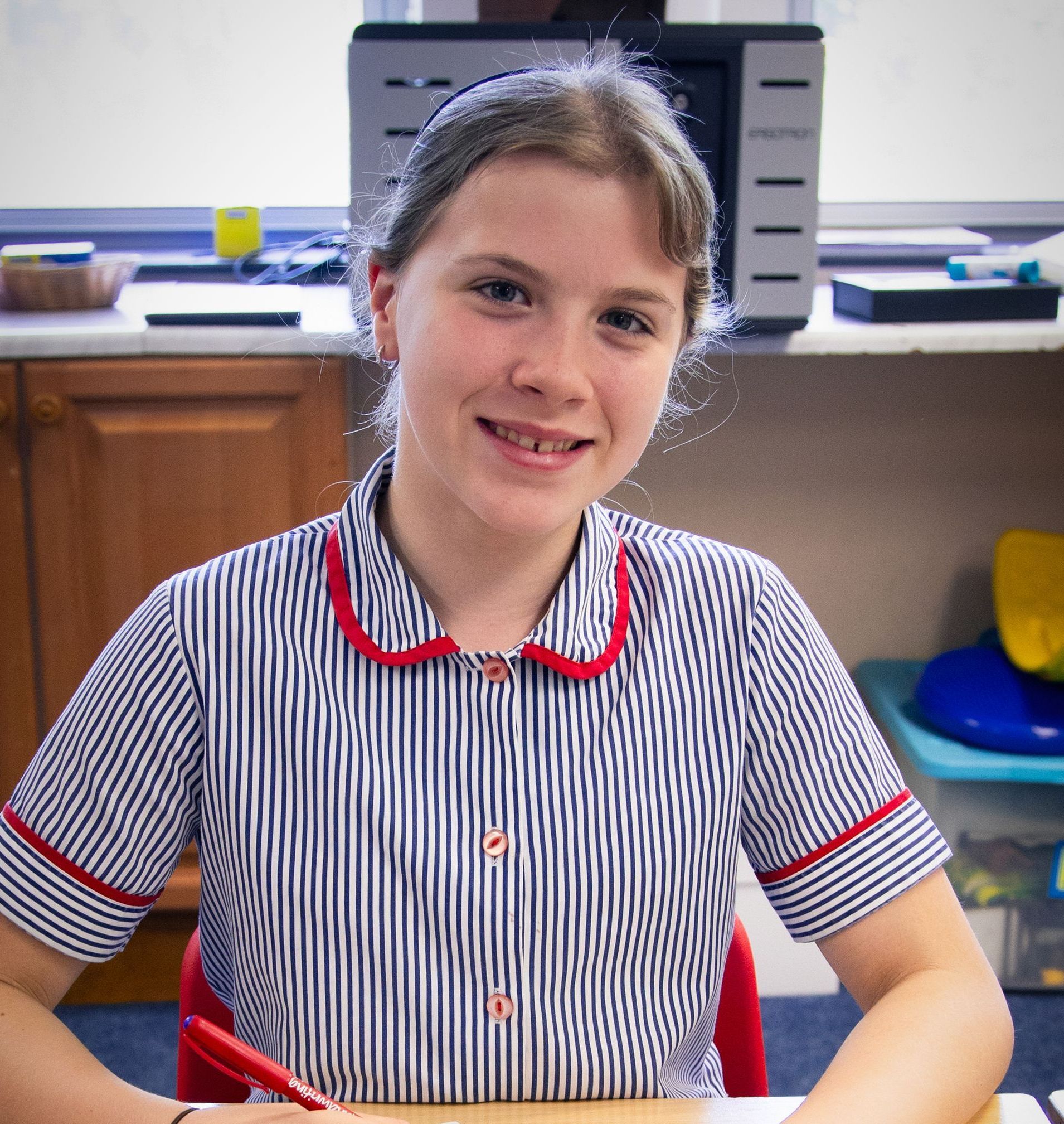 A girl in a striped shirt is smiling while sitting at a desk