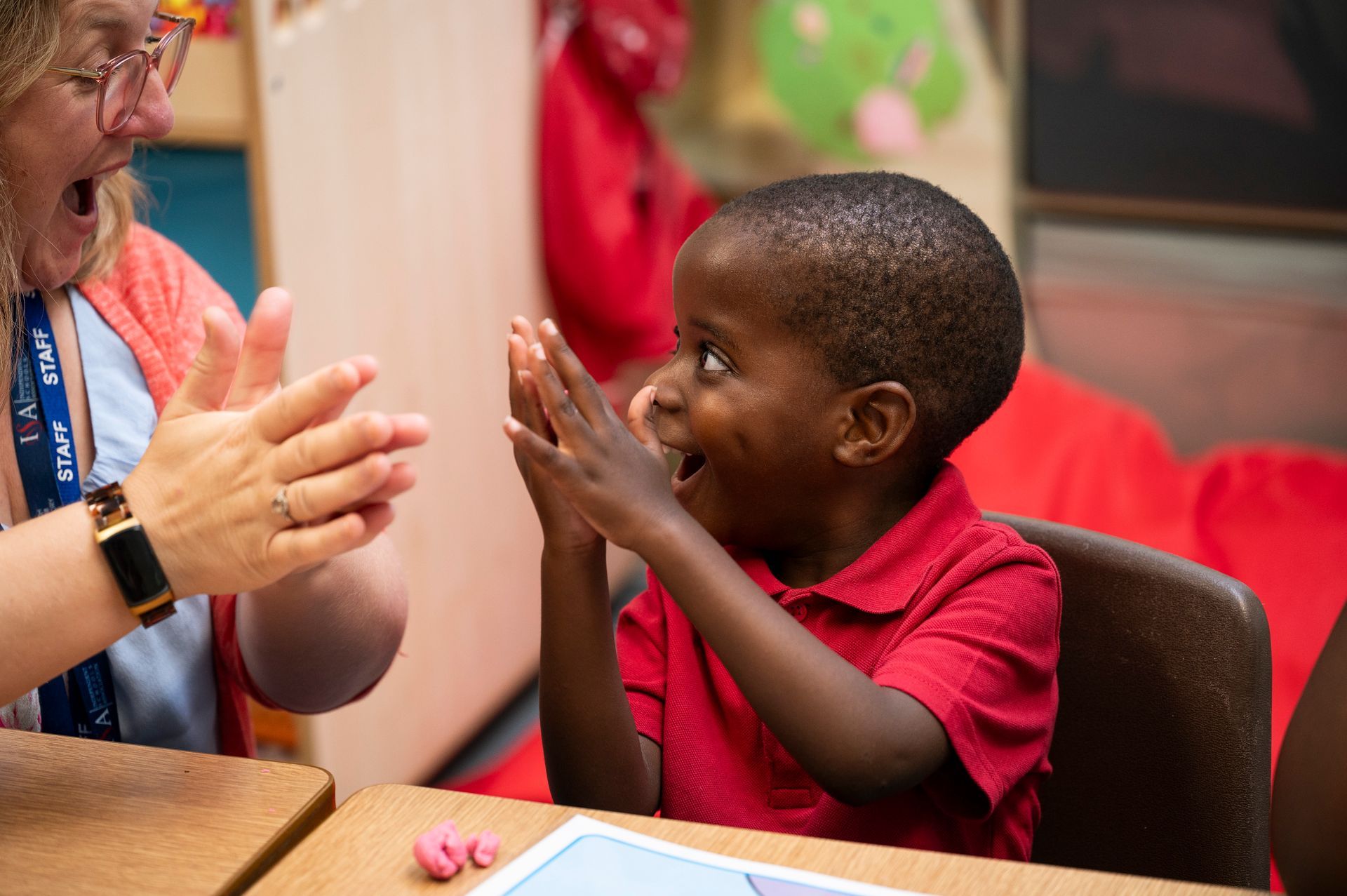 A woman is clapping hands with a young boy in a classroom.