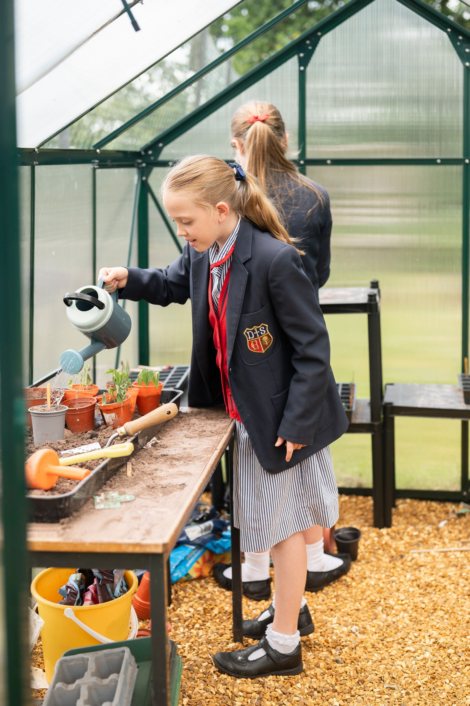A young girl is watering plants in a greenhouse.