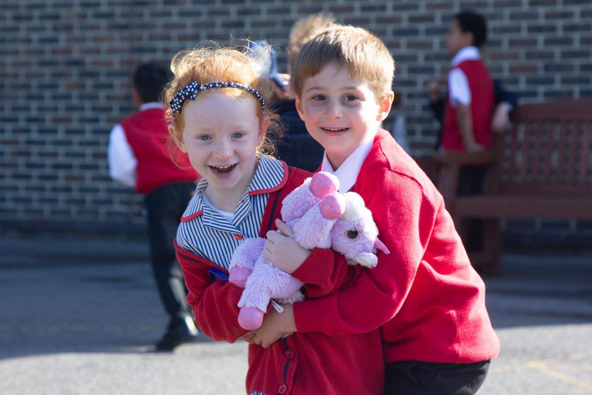 A boy and a girl are hugging and holding a stuffed animal