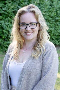 A woman wearing glasses and a sweater is smiling for the camera.