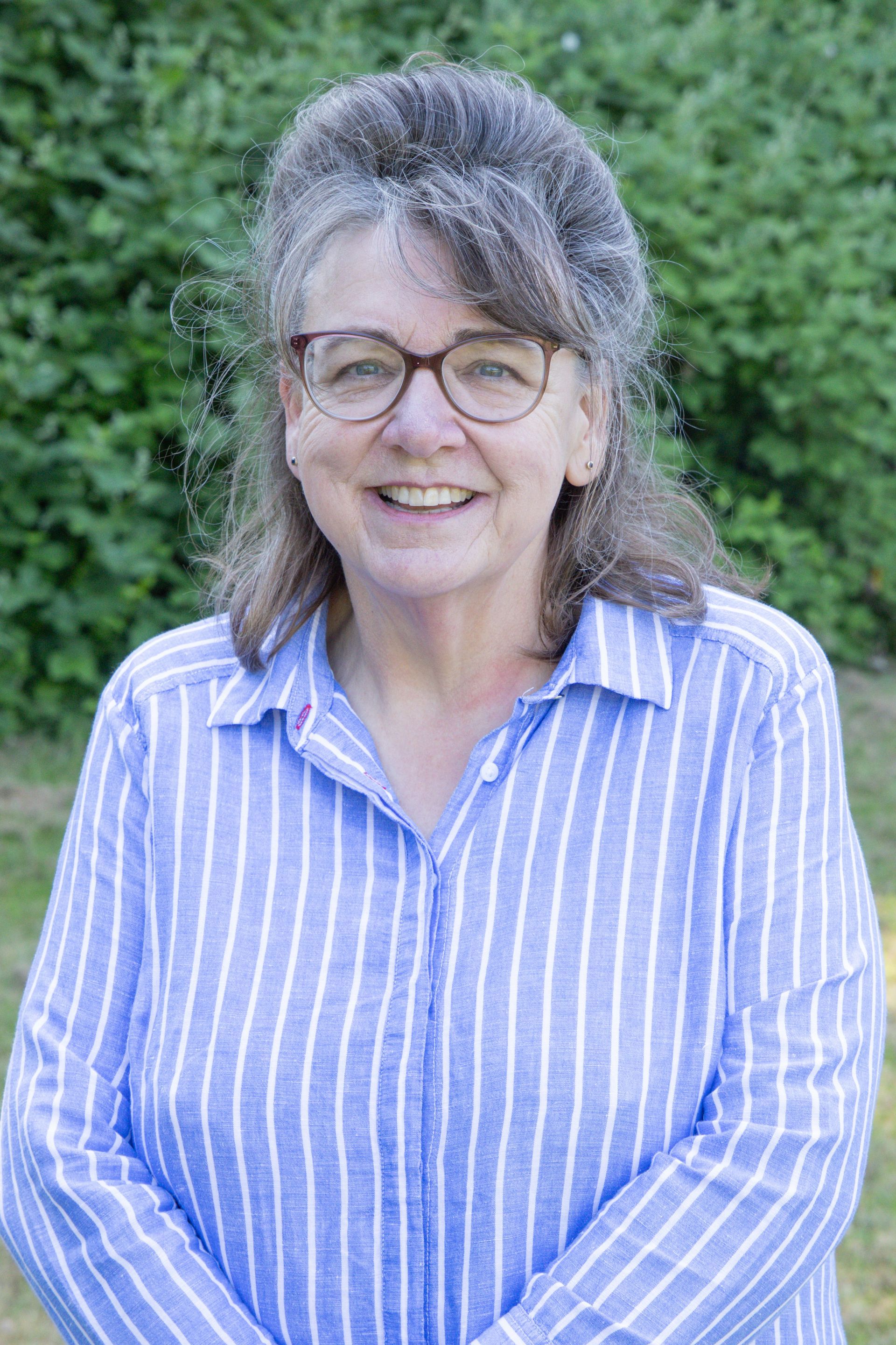 A woman wearing glasses and a blue and white striped shirt is smiling for the camera.