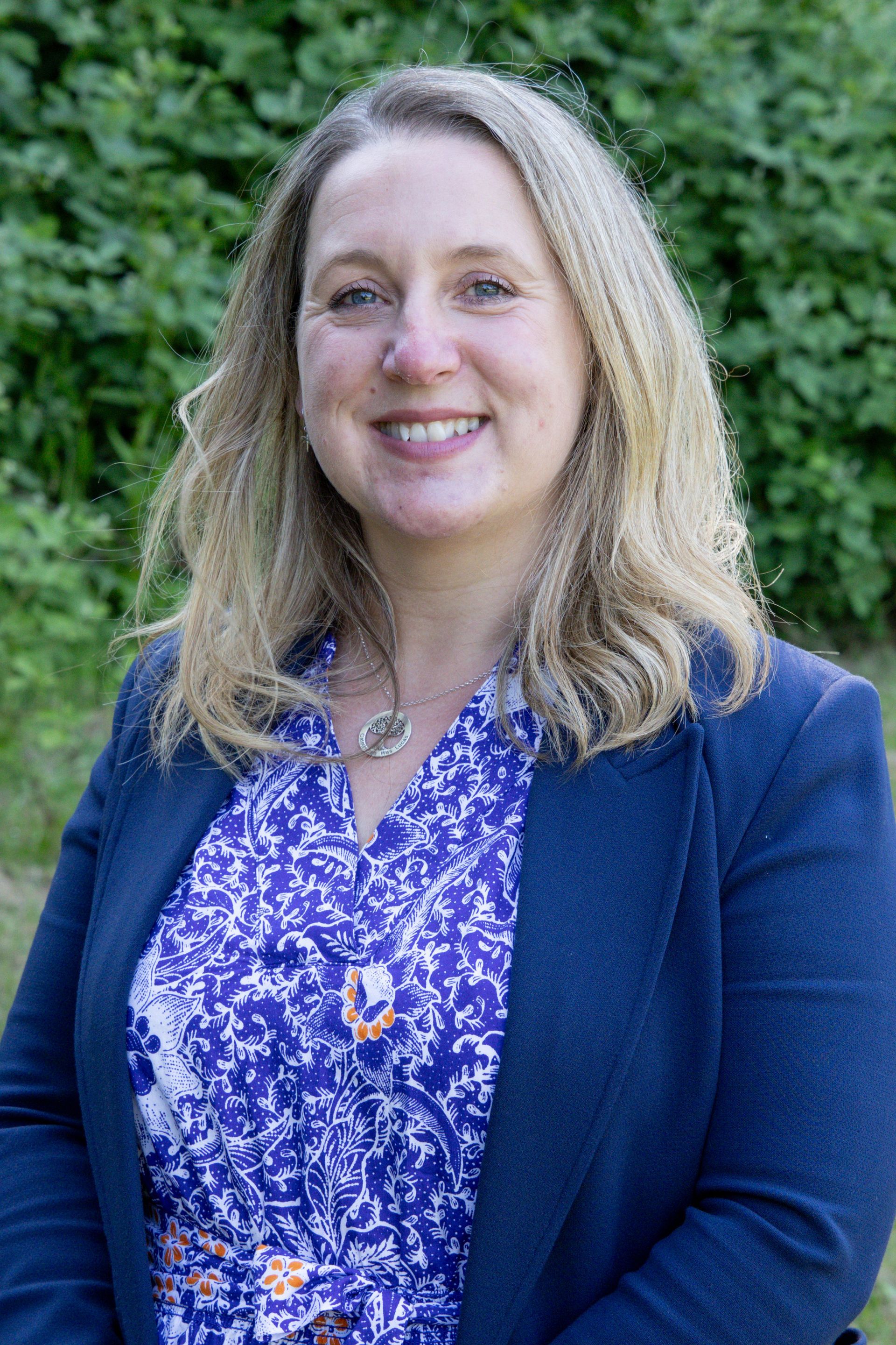 A woman in a blue jacket and purple shirt is smiling for the camera.