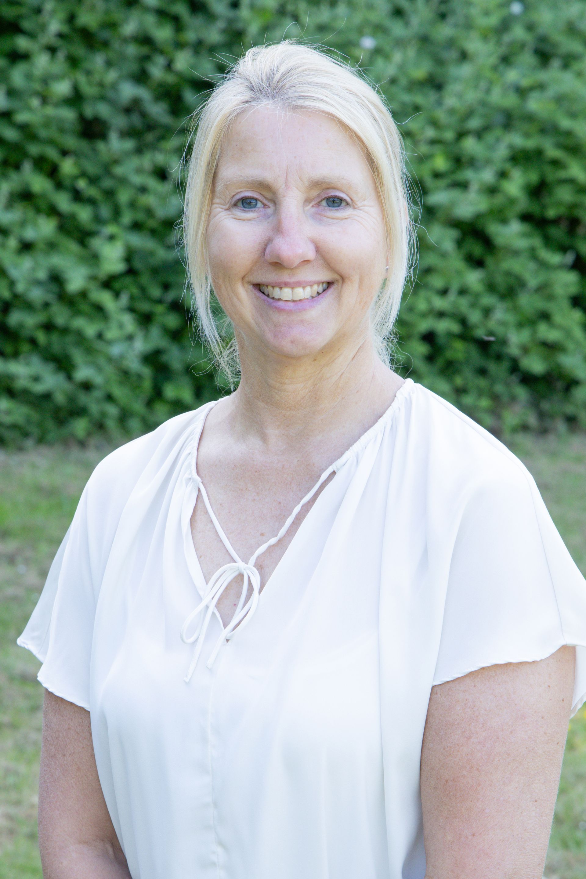 The woman is wearing a white shirt and smiling for the camera.
