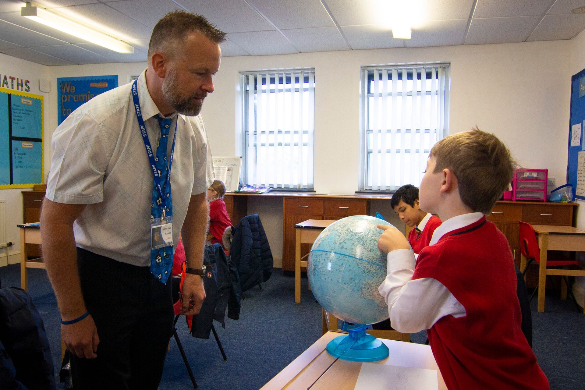 A man is standing next to a boy looking at a globe in a classroom.