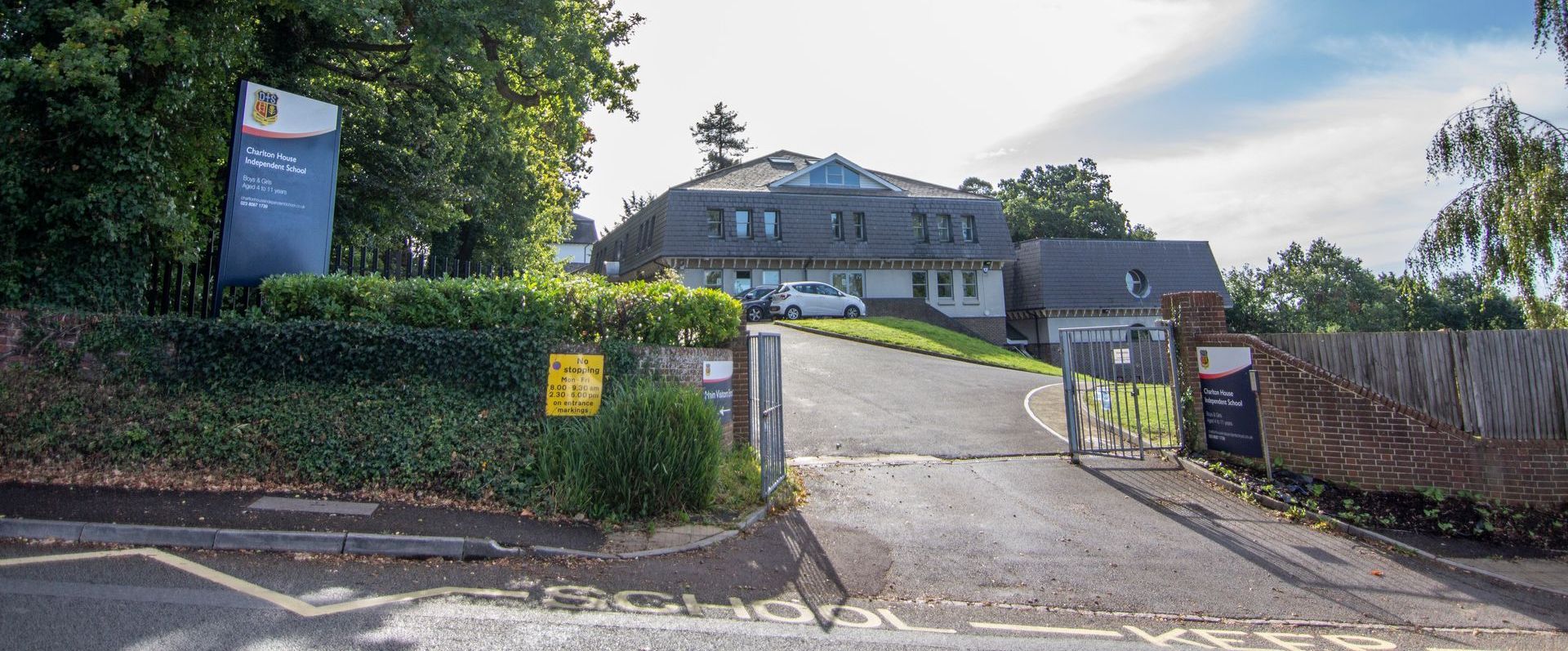 Entrance to Charlton House Independent School with a sign and a vehicle, surrounded by trees and a cloudy sky.