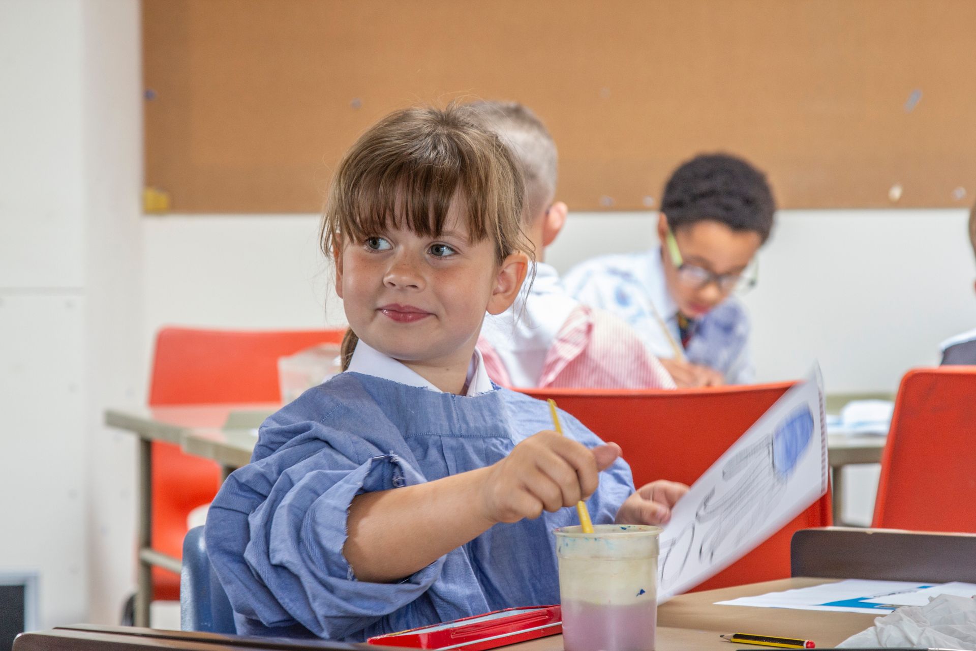 A young boy is sitting at a desk in a classroom with a pencil in his hand.
