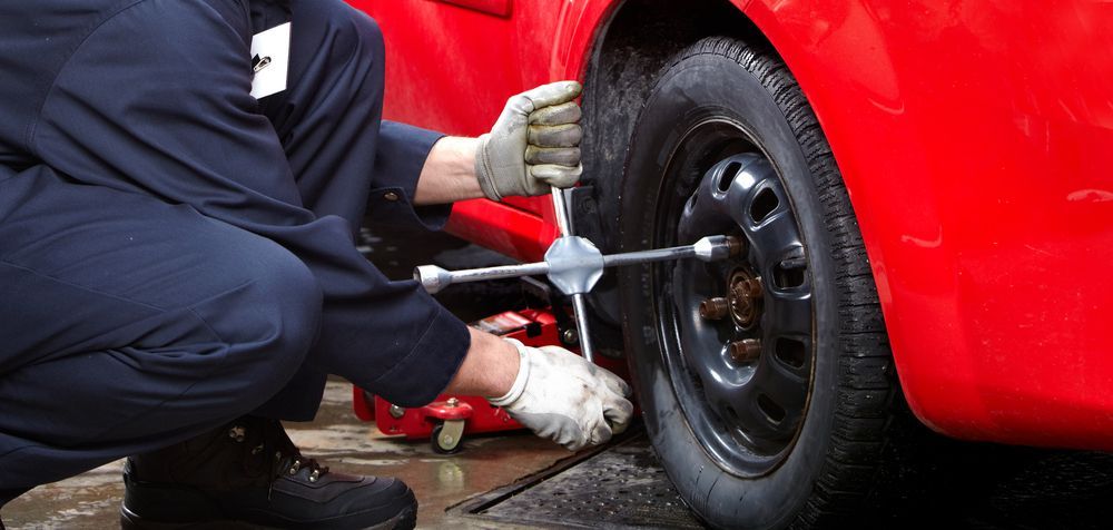 A Man Is Changing A Tire On A Red Car With A Wrench — Tamworth Muffler Man In Tamworth, NSW
