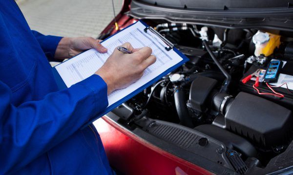 A Mechanic Is Writing On A Clipboard While Looking Under The Hood Of A Car — Tamworth Muffler Man In Tamworth, NSW