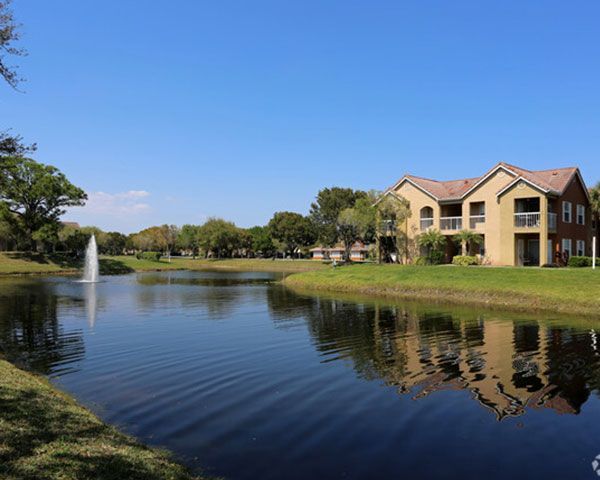 A lake with a fountain in the middle of it and a house in the background.