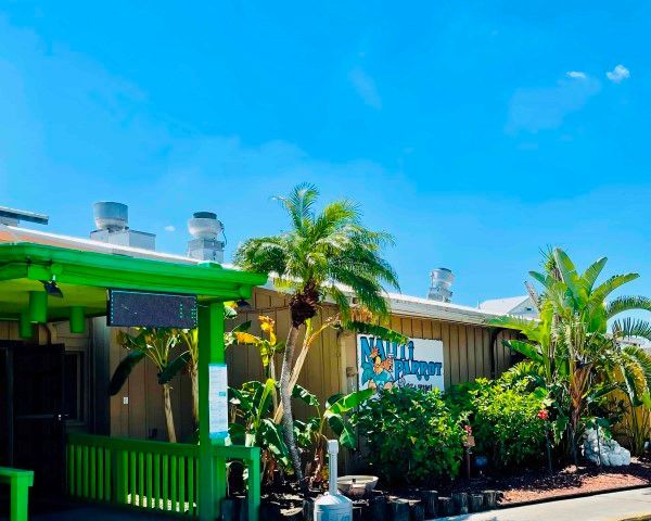 A restaurant with a green awning and palm trees in front of it.