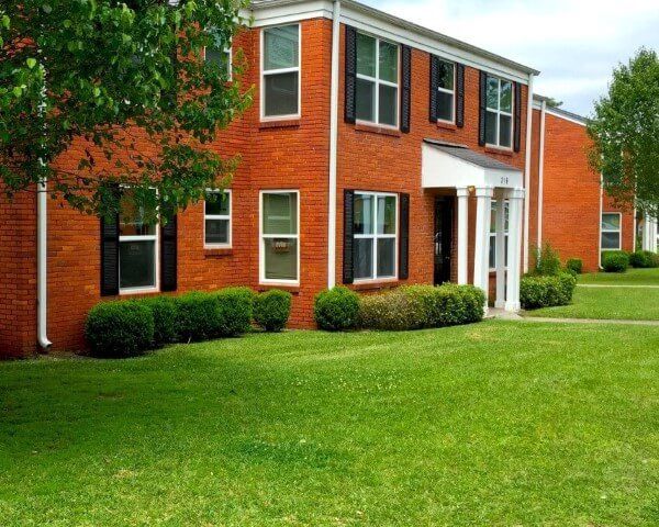 A brick apartment building with a lush green lawn in front of it.