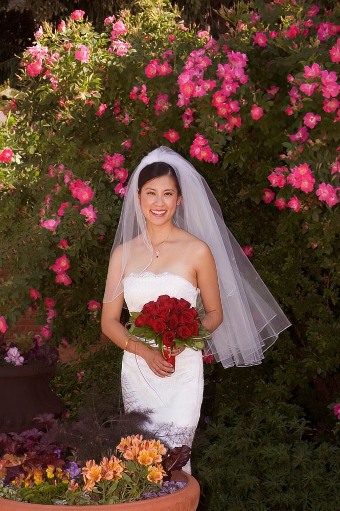 A bride in a white dress and veil is holding a bouquet of red roses.