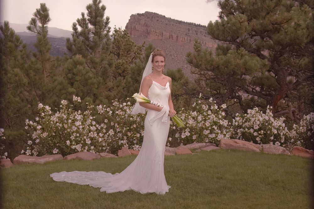 A woman in a wedding dress is standing in the grass holding a bouquet of flowers.