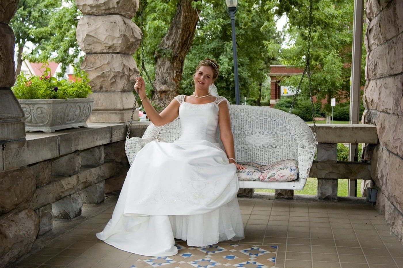 A woman in a wedding dress is sitting on a bench on a porch.