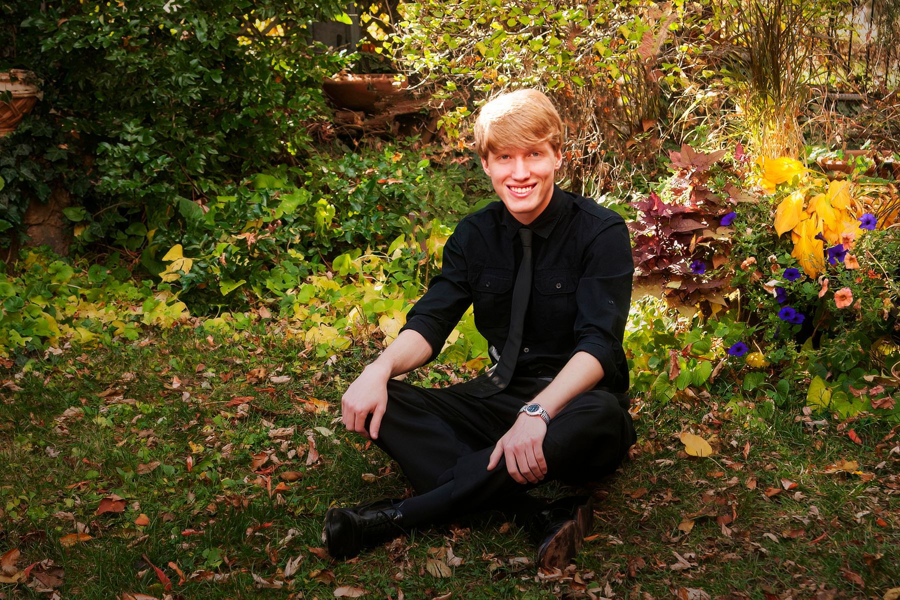 A man in a black shirt and tie is sitting on the grass