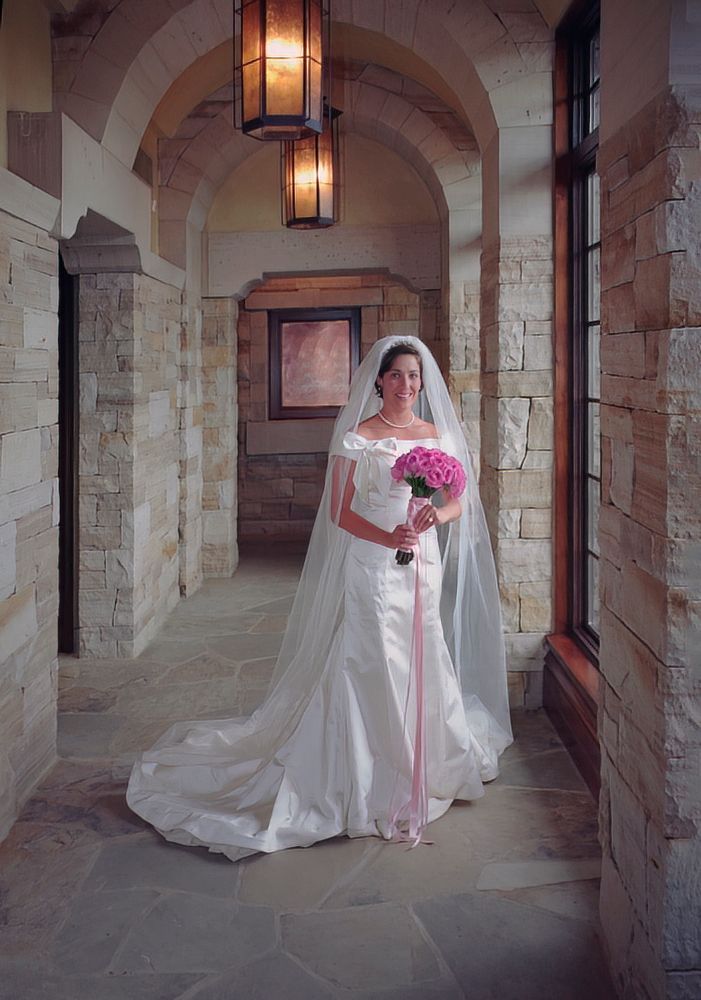 A woman in a wedding dress is standing in a hallway holding a bouquet of pink flowers.
