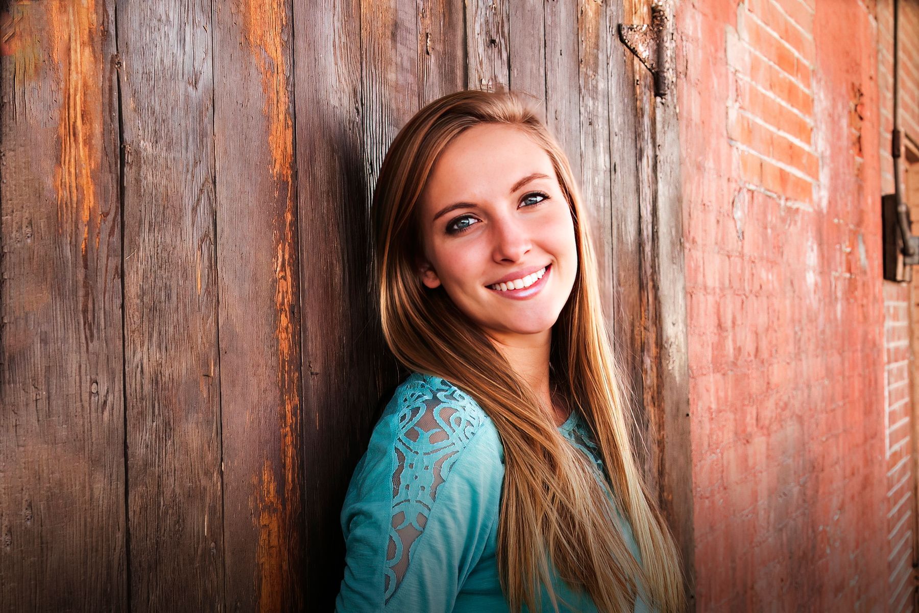 A young woman is leaning against a wooden wall and smiling.