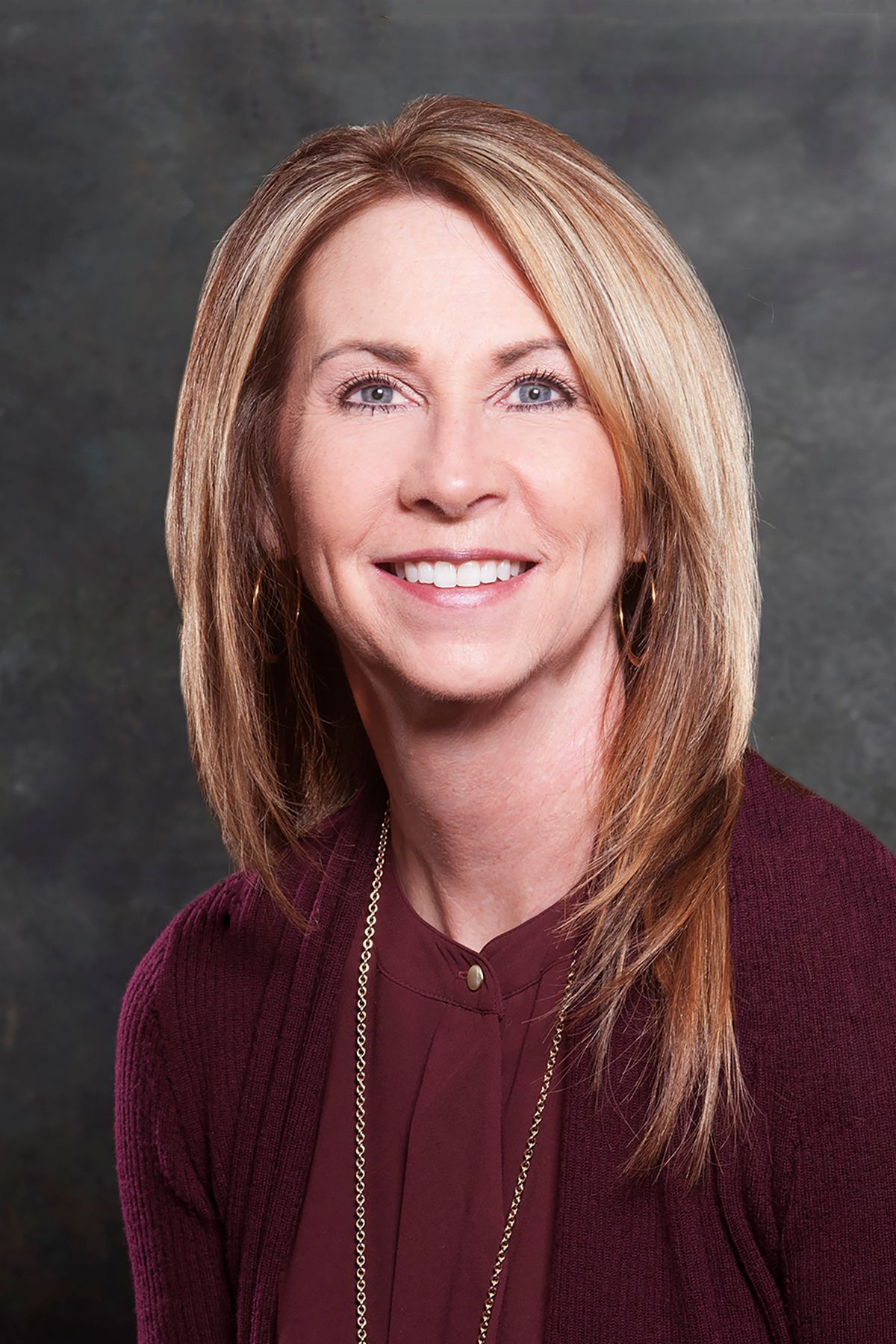 A woman wearing a purple sweater and a necklace is smiling for the camera.