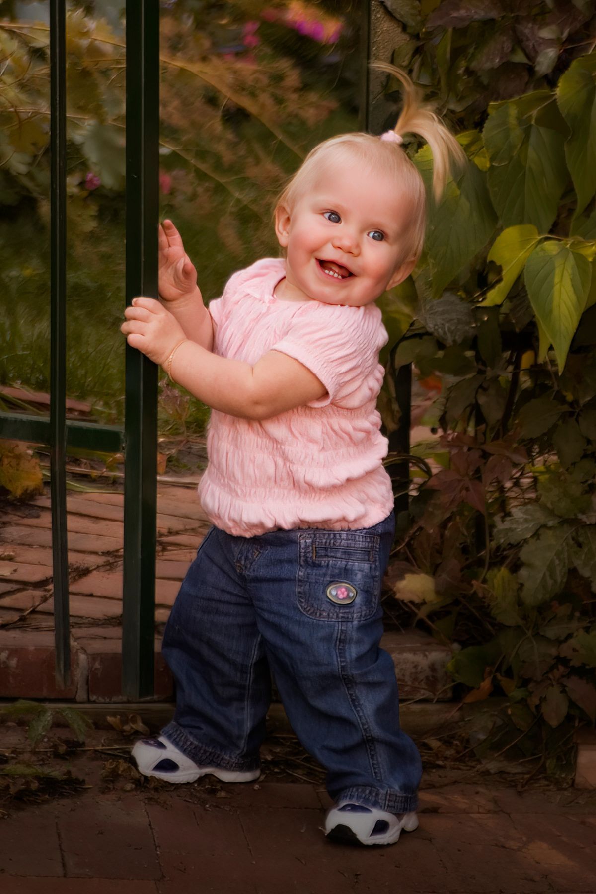 A little girl is standing next to a fence and smiling.