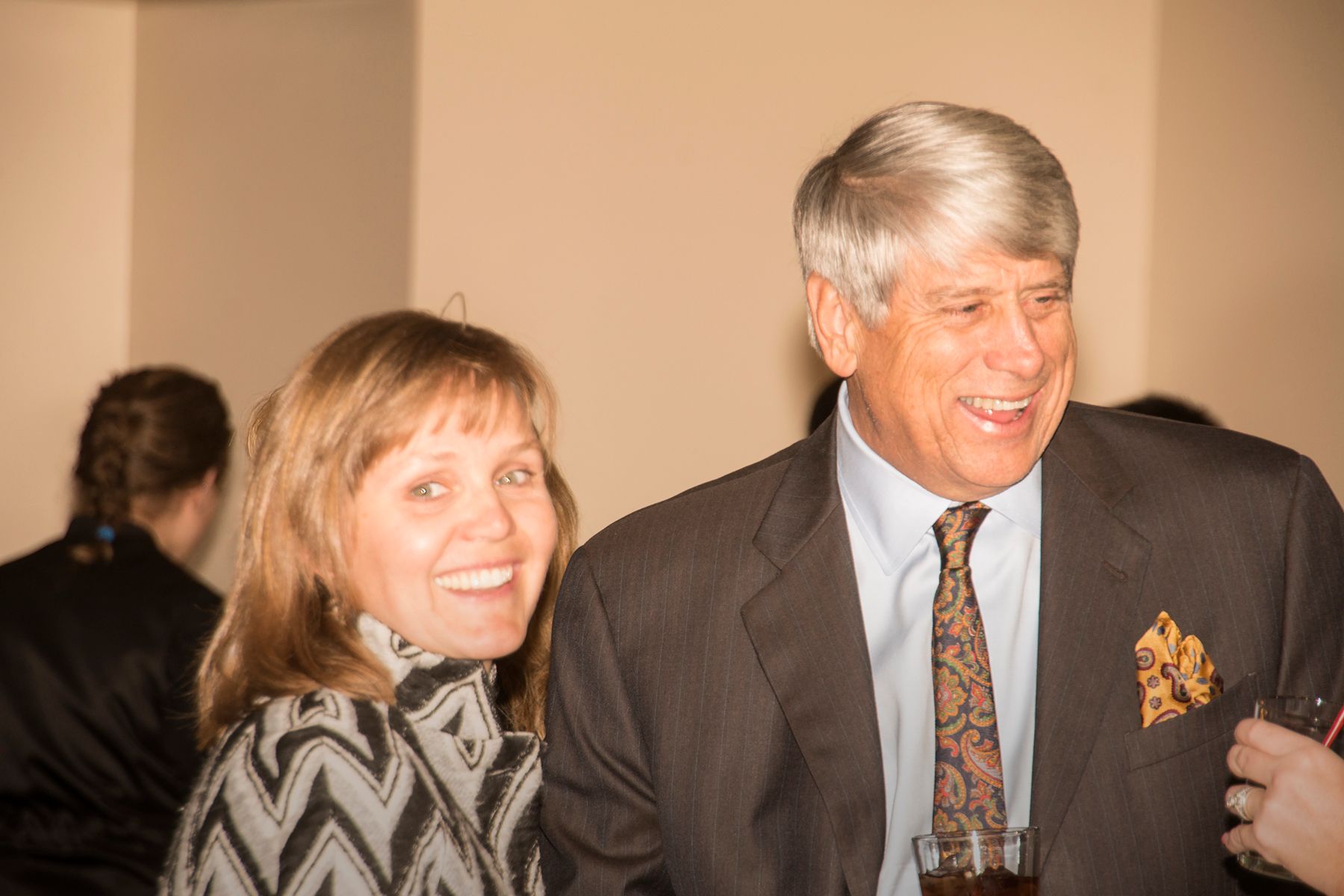 A man and a woman are standing next to each other and smiling . the man is wearing a suit and tie.
