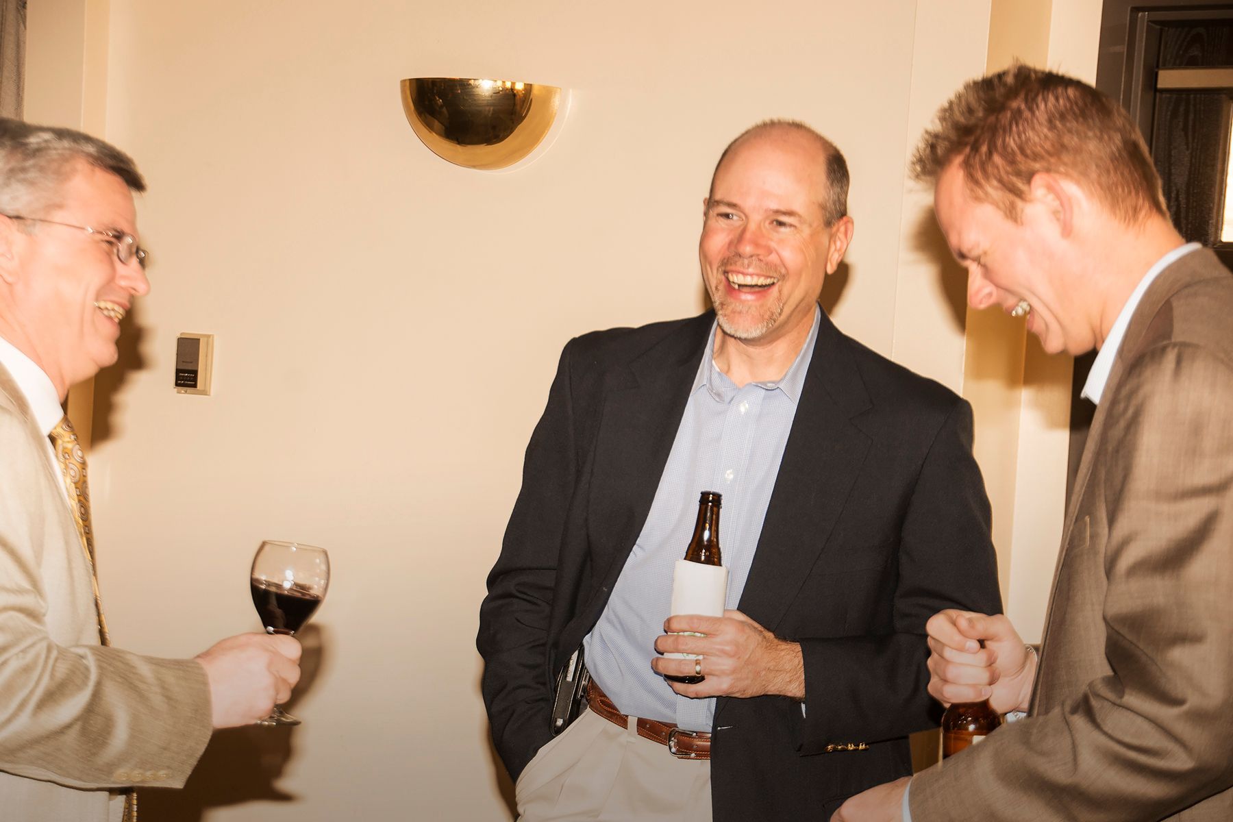 Three men are laughing and drinking wine in a room