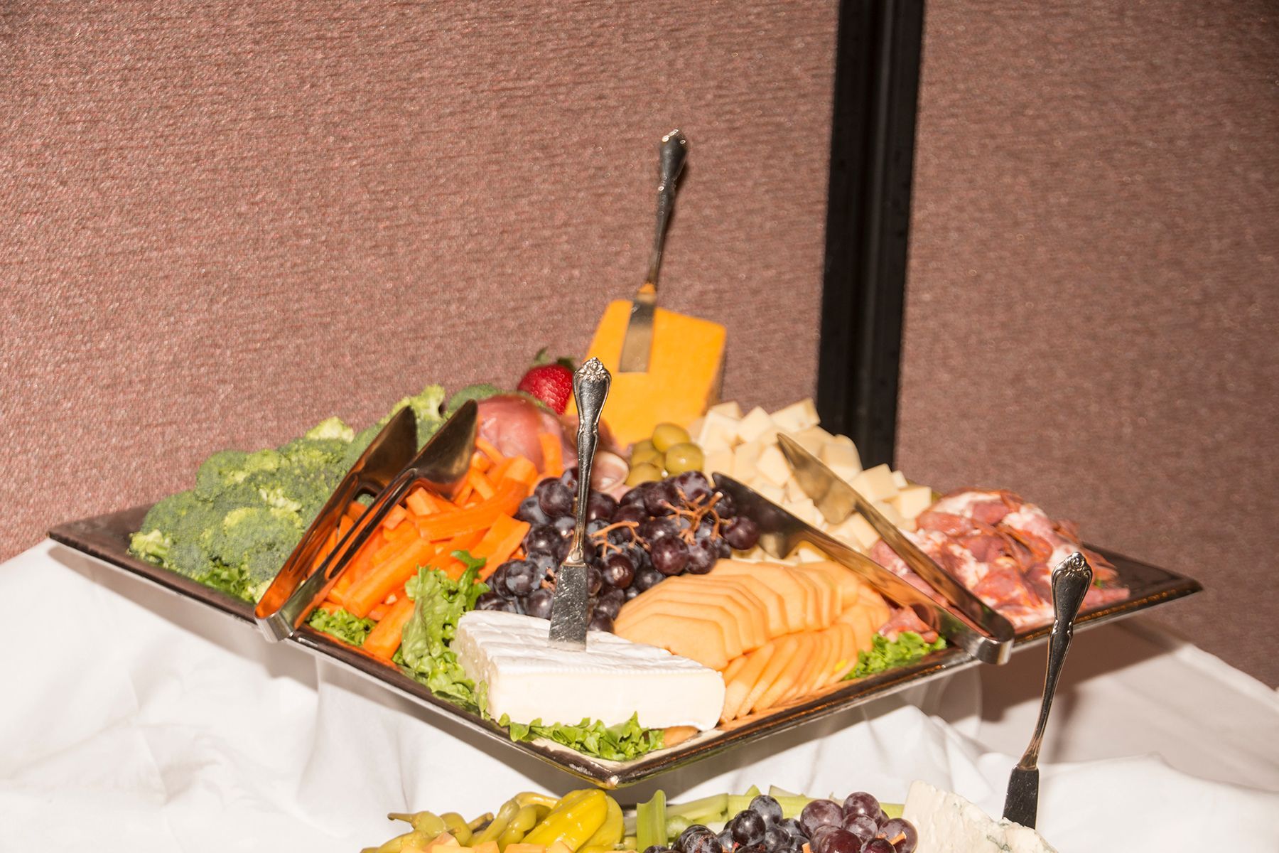 A tray of fruits and vegetables on a table with tongs.