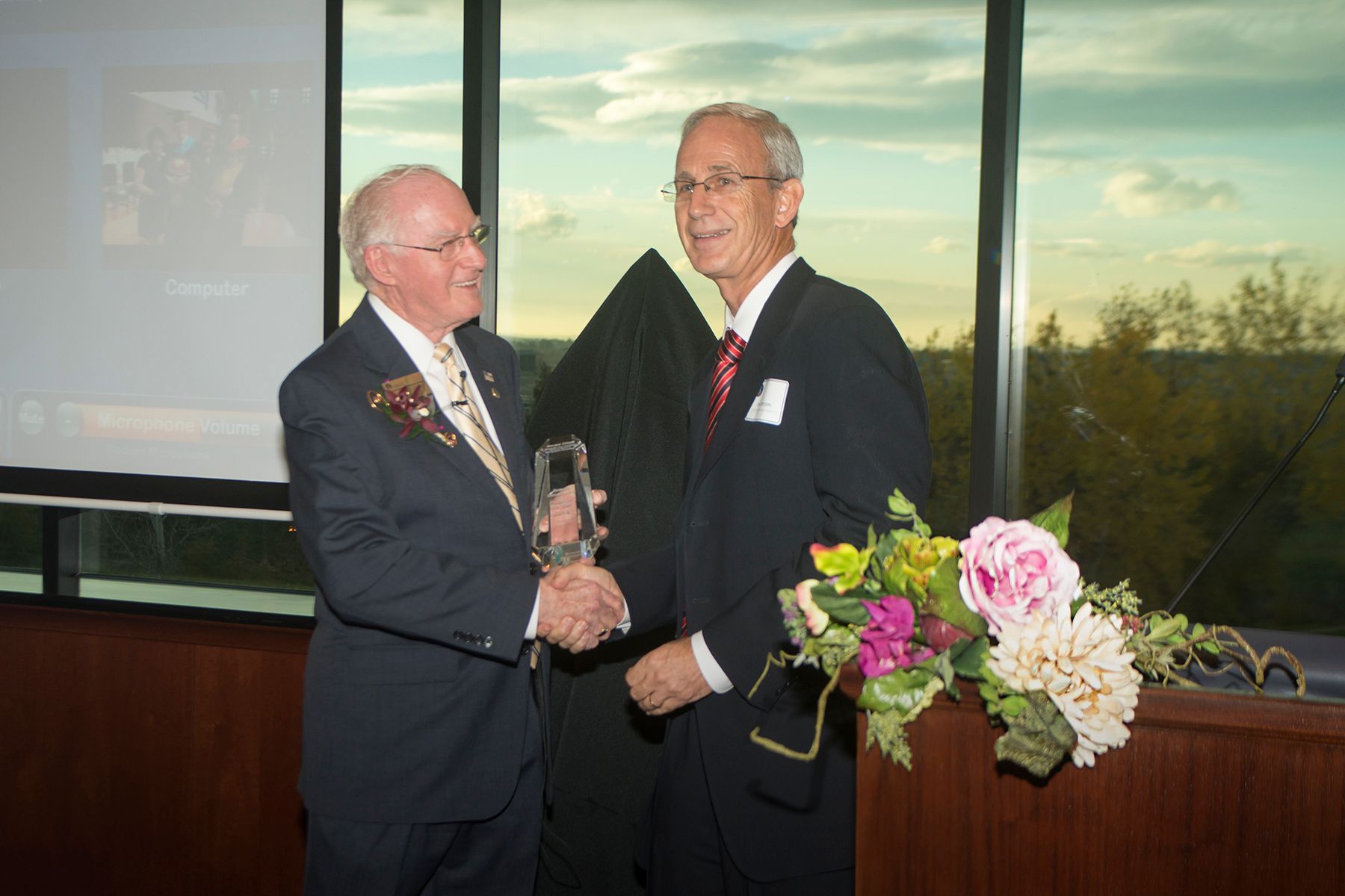 Two men in suits shaking hands in front of a window