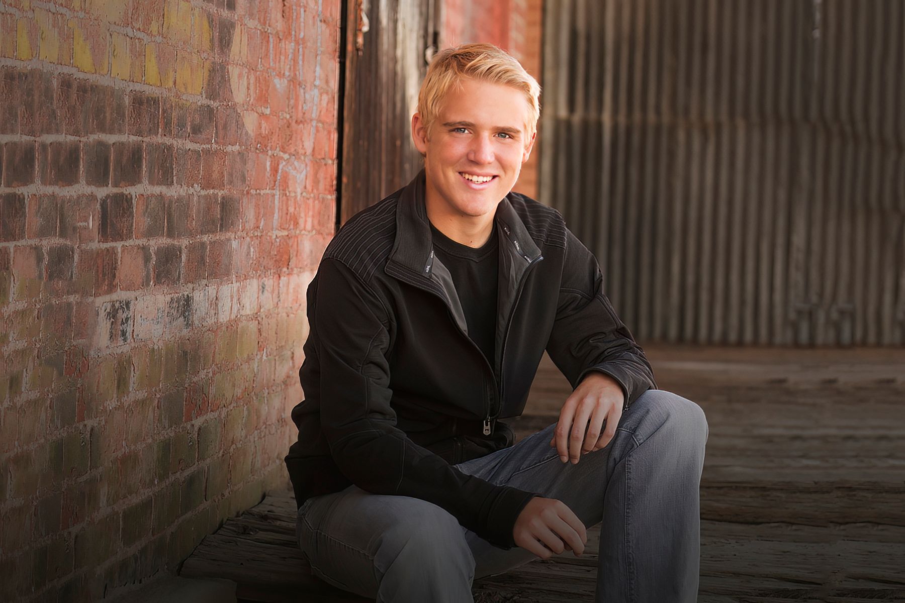 A young man is sitting in front of a brick wall.