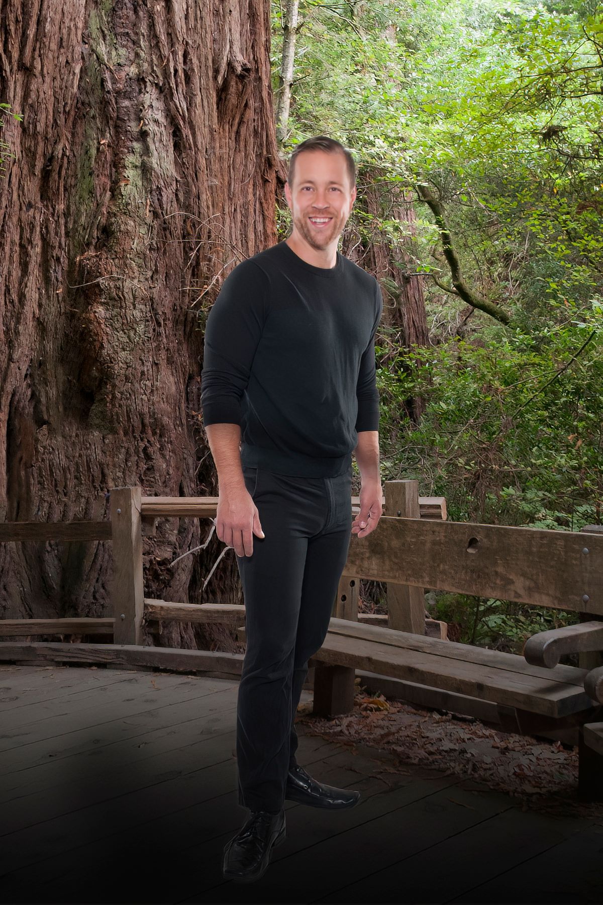 A man in a black shirt is standing in front of a large tree.