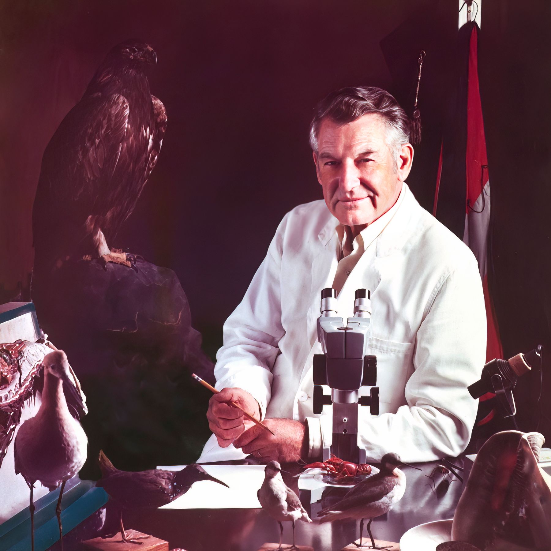 A man in a lab coat is sitting at a desk with stuffed birds and a microscope