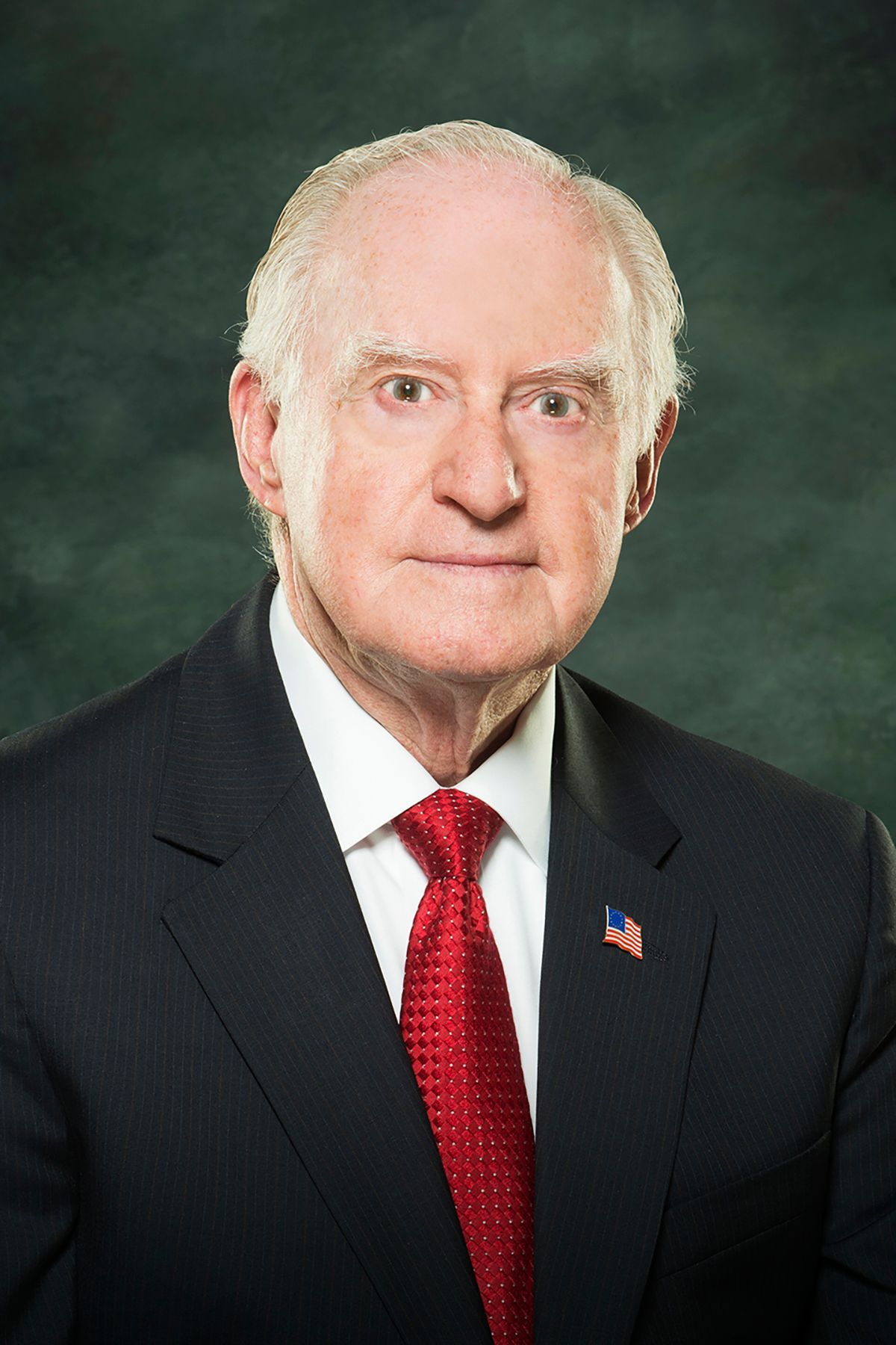 A man in a suit and tie is standing in front of a green background.