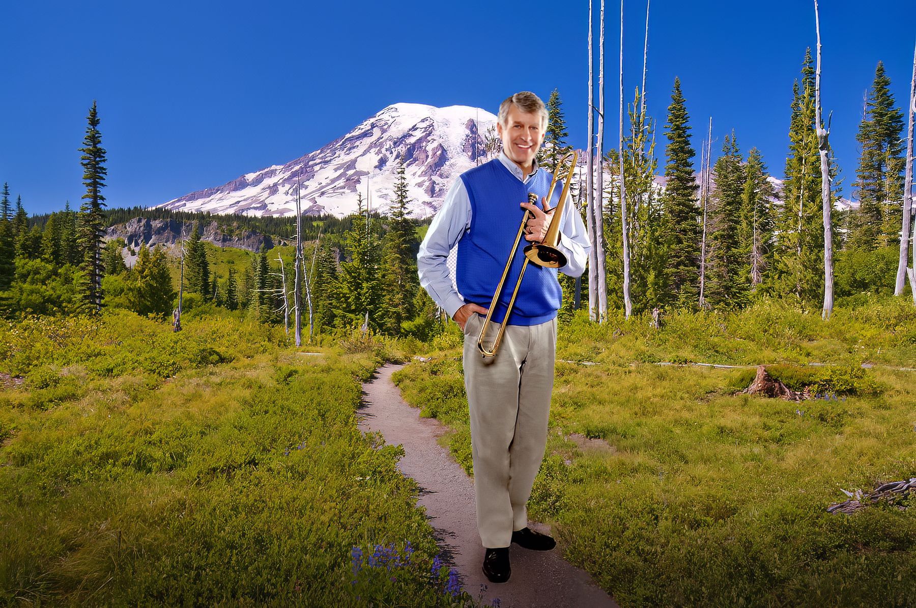 A man playing a trombone in a field with a mountain in the background