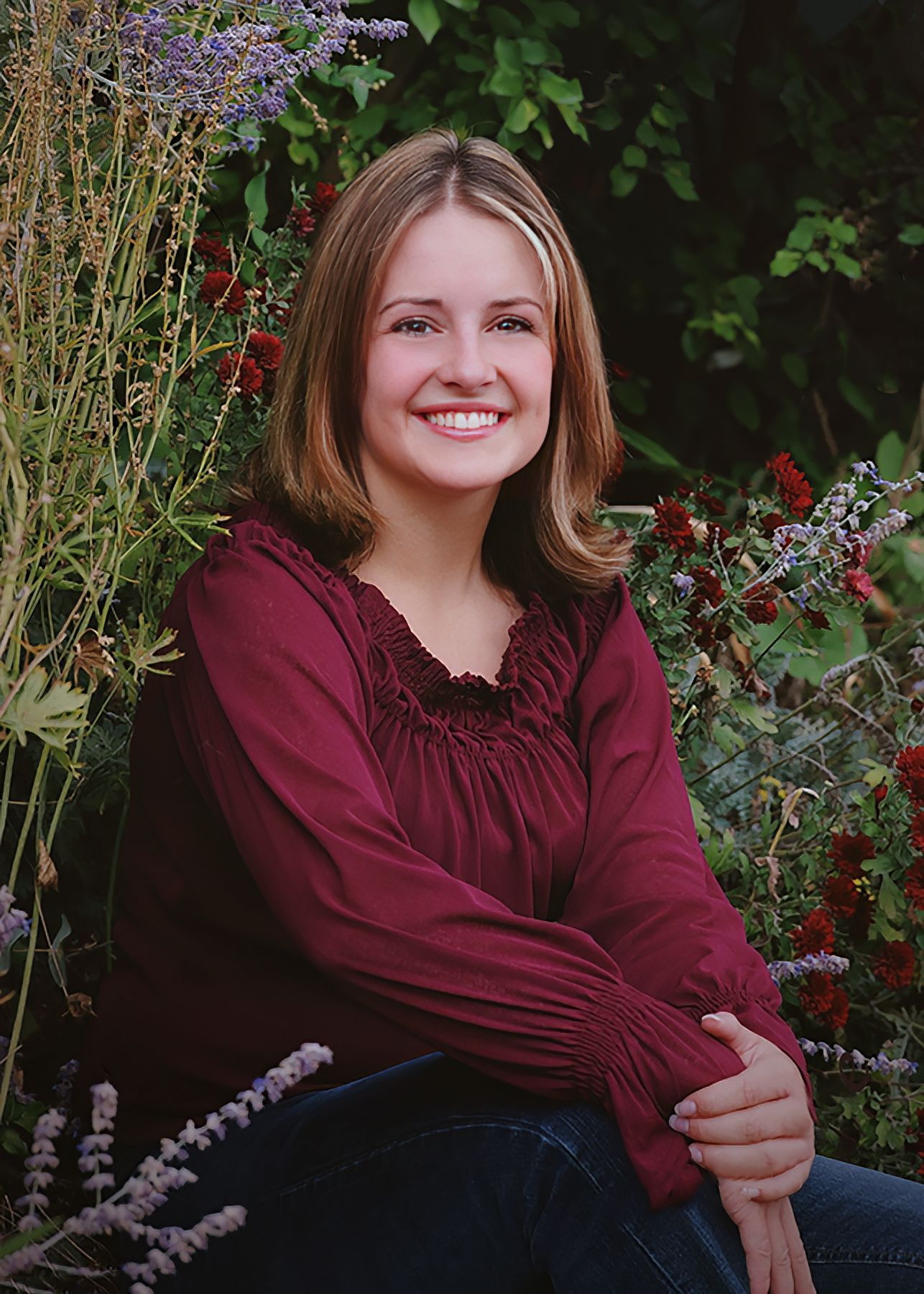 A woman in a maroon shirt is sitting in front of flowers