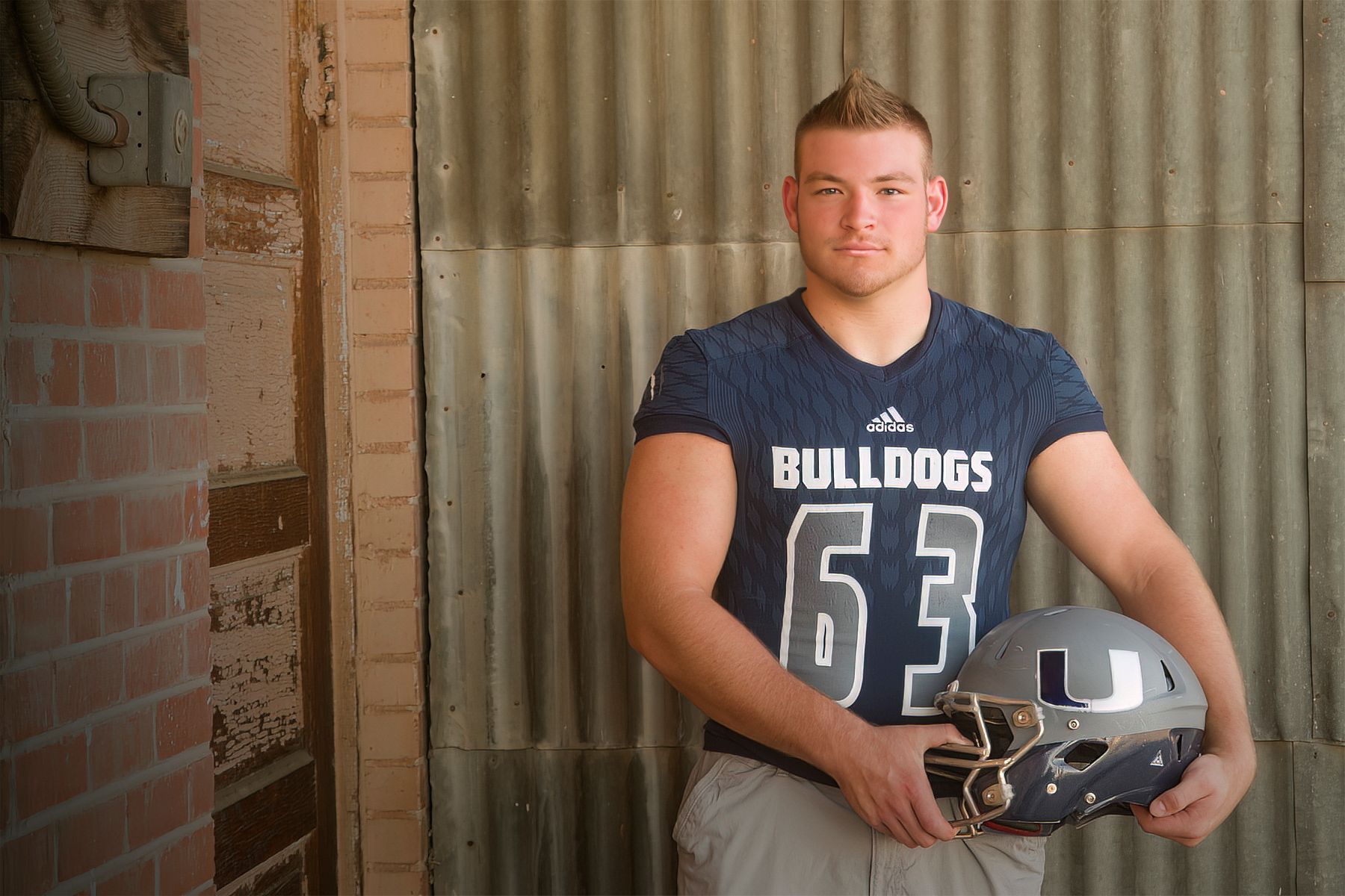 A young man in a bulldog jersey is holding a football helmet.