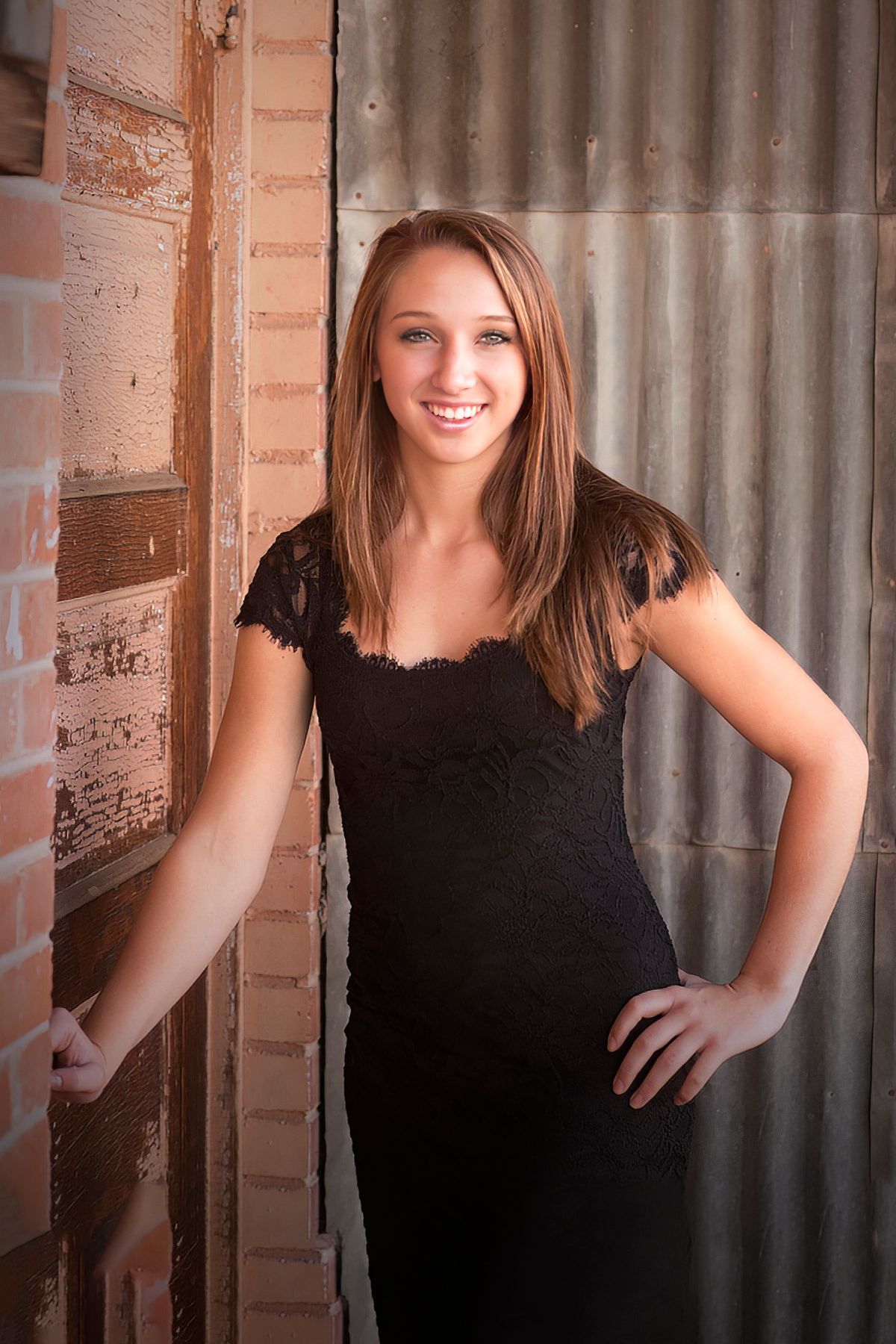 A woman in a black dress is standing next to a brick wall.