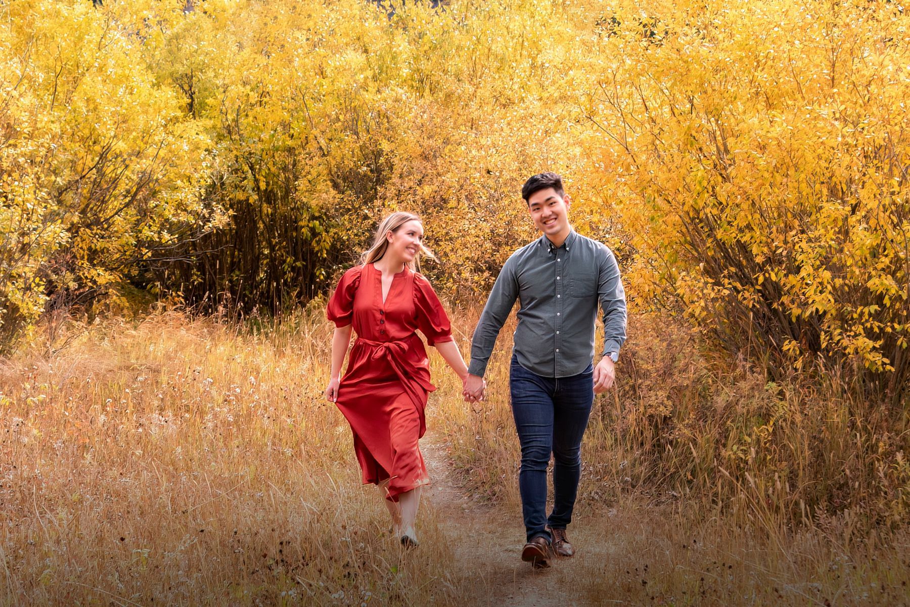 A man and a woman are walking through a field holding hands.