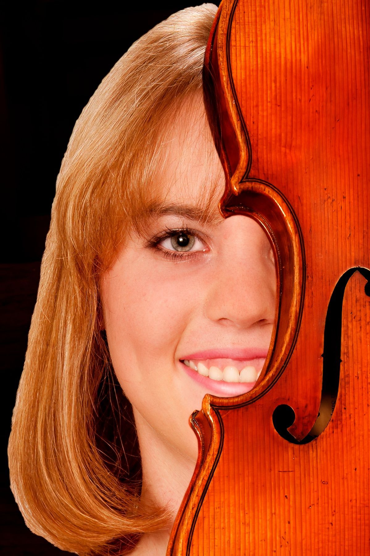 A woman is smiling while holding a violin in front of her face