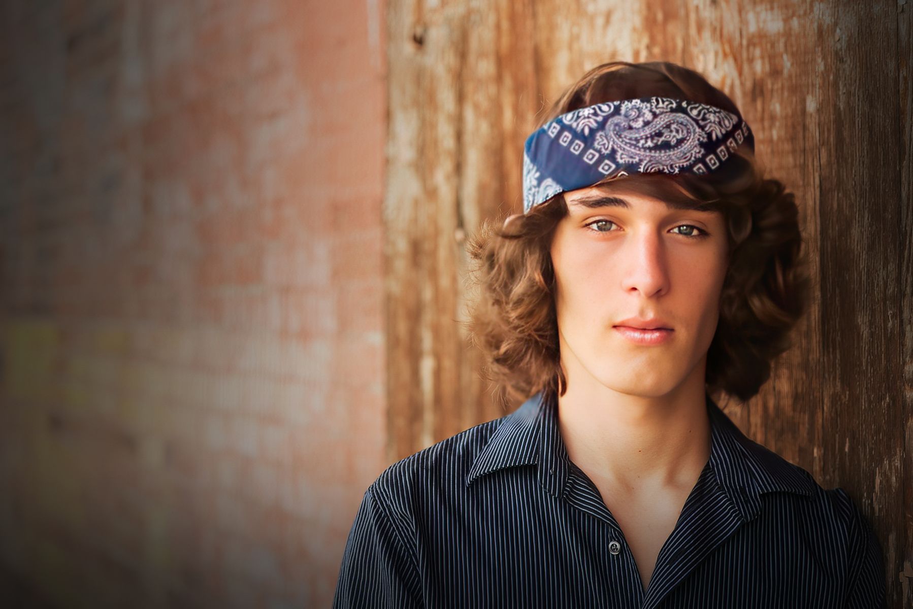 A young man wearing a bandana is leaning against a wooden wall.