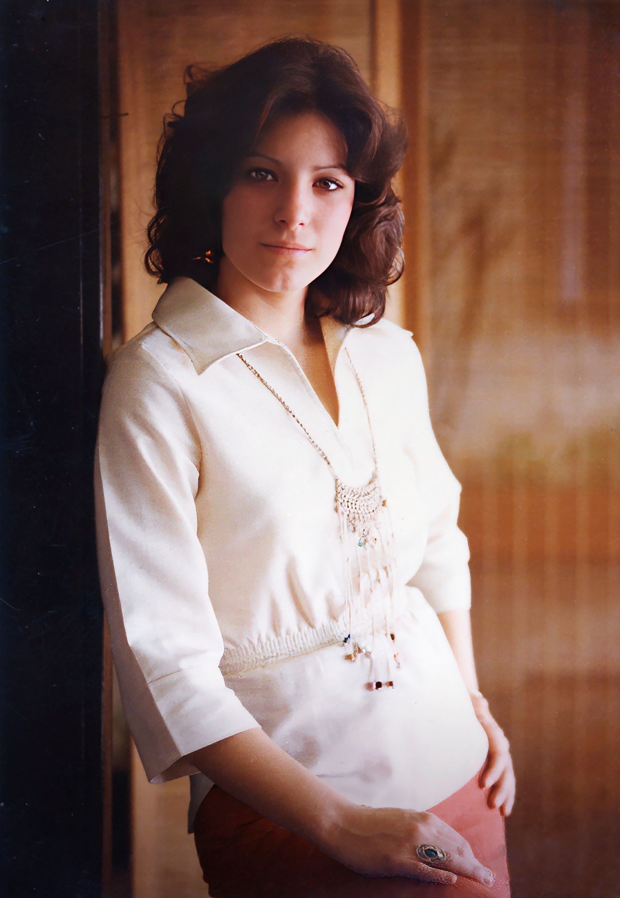 A woman in a white shirt is standing in front of a wooden wall